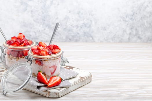 Parfait with Fresh Strawberries, Yoghurt and Crunchy Granola in Transparent Glass Mason Jars on White Rustic Wooden Background Angle View, Healthy Breakfast or Light Summer Dessert, Copy Space