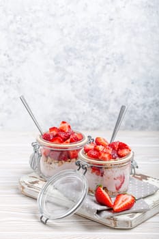 Parfait with Fresh Strawberries, Yoghurt and Crunchy Granola in Transparent Glass Mason Jars on White Rustic Wooden Background Angle View, Healthy Breakfast or Light Summer Dessert, Copy Space