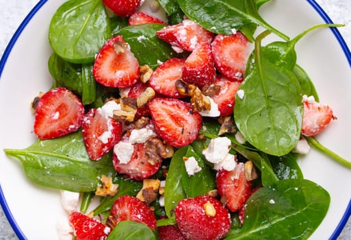 Close Up of Light Healthy Summer Salad with fresh Strawberries, Spinach, Cream Cheese and Walnuts on White Ceramic Plate, white rustic stone Background Top View.