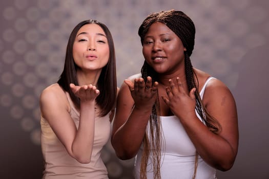 African american and asian women with different body types and ethnicity sending air kiss. Diverse beauty models showing love and affection gesture and posing together in studio