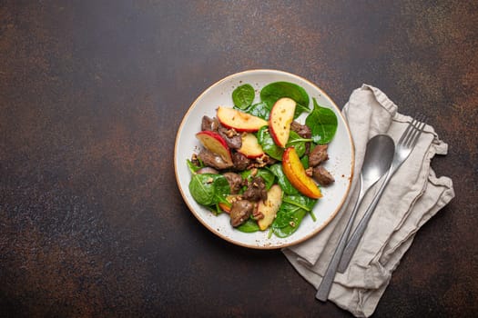 Healthy Salad with Iron Rich Ingredients Chicken Liver, Apples, Fresh Spinach and Walnuts on White Ceramic Plate, Dark Brown Rustic Stone Background Top View Copy Space.