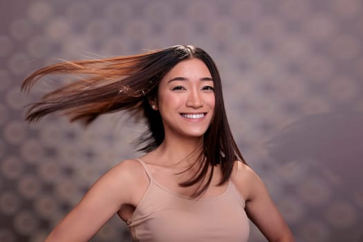 Happy asian woman with shiny fluttering hair after haircare routine procedures smiling and looking at camera. Confident optimistic young lady with smooth hairstyle portrait