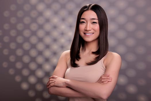 Confident attractive asian woman posing with crossed hands portrait. Smiling cheerful beautiful model standing in beige top, feeling happy and expressing successful gesture