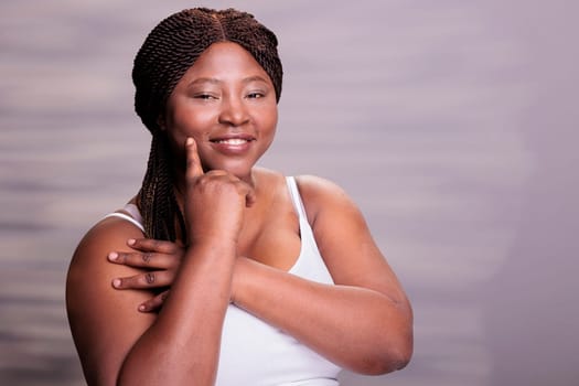 Natural beautiful skincare body positive model touching cheek portrait. African american curvy woman pointing on perfect healthy skin, holding finger on face and looking at camera