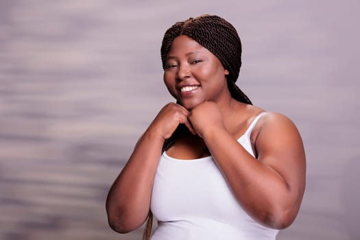 Body positive woman showing self love and care, holding arms under face portrait. Smiling confident plus size african american lady expressing happiness and looking at camera