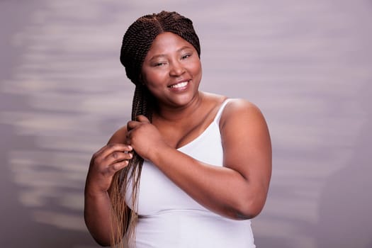 African american woman showing hair braiding technique, making african hairstyle tutorial. Natural beautiful plus size model smiling, looking at camera with carefree facial expression