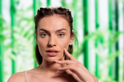 Young caucasian skincare model posing with fingers on face portrait. Natural beautiful woman showing glowing skin after organic cosmetology treatment on bamboo background