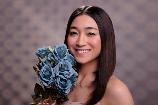 Smiling happy asian woman posing with flowers bouquet gift portrait. Girl with cheerful facial expression holding blue roses bunch in hands and looking at camera close up