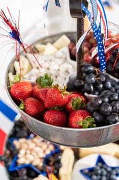 July 4th charcuterie board on a two-tiered serving metal stand filled with cheese, crackers, salami, and fresh fruits