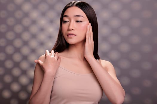 Skincare asian model with natural make up posing for portrait, holding arms on face and looking to side. Beautiful young woman with healthy clean glowing skin wearing beige top