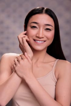 Young smiling asian woman touching face and showing natural beauty concept. Pretty model holding fingers on cheek and checking smooth fresh hydrated skin after skincare procedures