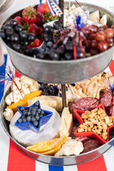 July 4th charcuterie board on a two-tiered serving metal stand filled with cheese, crackers, salami, and fresh fruits