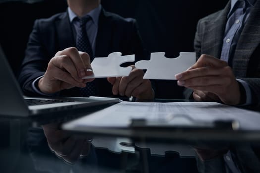 two businessmen holding two jigsaw puzzle pieces connecting a pair of puzzle pieces for matching goals, success and starting a new project in the office. Business concept.