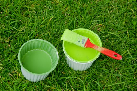 two buckets with green paint and one red brush with green paint on the grass. High quality photo