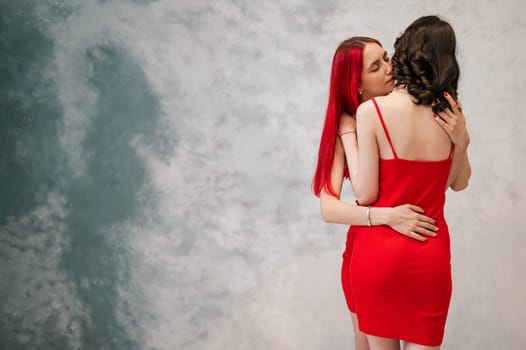 A close-up portrait of two tenderly embracing women dressed in identical red dresses. Lesbian intimacy