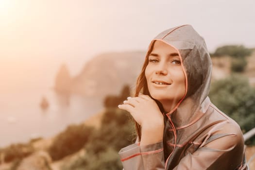 Woman rain park. Happy woman portrait wearing a raincoat with transparent umbrella outdoors on rainy day in park near sea. Girl on the nature on rainy overcast day