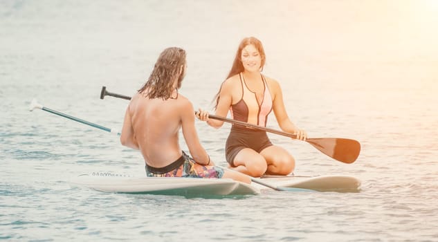 Sea woman and man on sup. Silhouette of happy young woman and man, surfing on SUP board, confident paddling through water surface. Idyllic sunset. Active lifestyle at sea or river