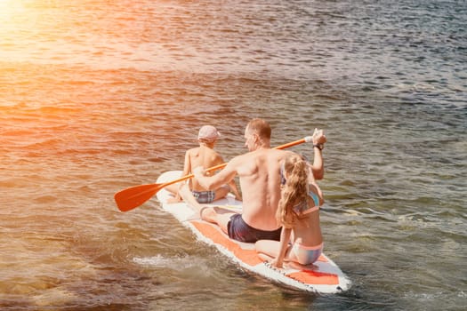 Father and his adorable little son and daughter sitting on stand up board having fun during summer beach vacation