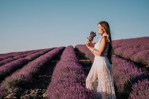 Close up portrait of young beautiful woman in a white dress and a hat is walking in the lavender field and smelling lavender bouquet.