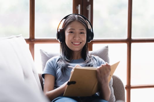 Online education, e-learning. Asian woman in stylish casual clothes, studying using a laptop, listening to online lecture, taking notes, online study at home.