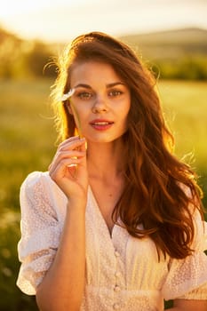 close portrait of a beautiful, laughing woman in a light dress holding a camomile near her face. High quality photo