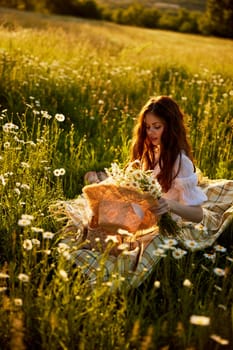 a beautiful woman in a light dress sits in a field of daisies at sunset holding a hat in her hands. High quality photo