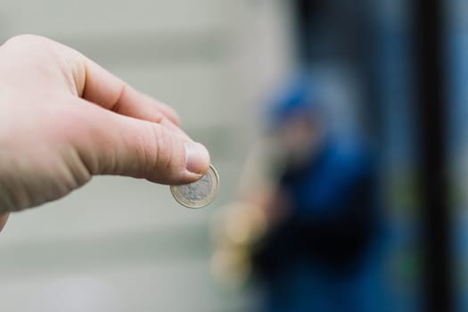 Street old performer musician plays saxofon blurred, coin in a hand focused