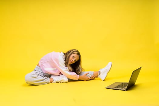 Fitness online. Girl doing stretching exercise on a floor alone with laptop at studio