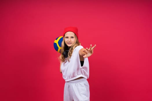 A teenager girl holds volleyball ball in hand and smiles on red yellow background. Studio photo.