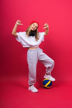 A teenager girl holds volleyball ball in hand and smiles on red yellow background. Studio photo.
