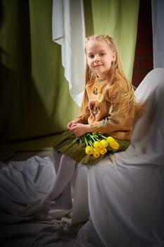 Portrait of a little blonde girl with bouquet of spring yellow flowers on a light background. Child in green dress holding a bouquet of tulips in hands. Spring concept