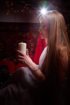 Beautiful arabian girl with candles in red room full of rich fabrics and carpets in sultan harem. Photo shoot of woman an oriental style odalisque. Model poses in sari as caring wife and hostess