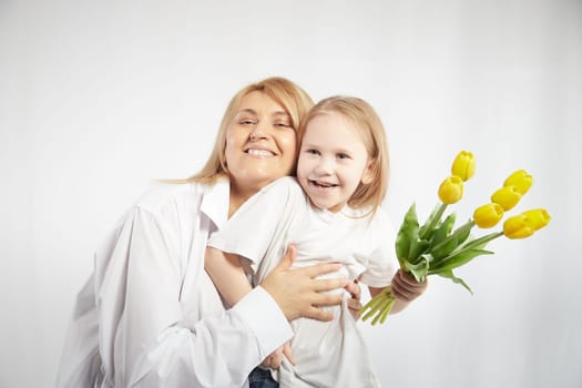 Blonde mother and daughter with a bouquet of tulips on a white background. Mom and girl together on holiday mother's day with flowers. Congratulations to women on International Women's Day on March 8