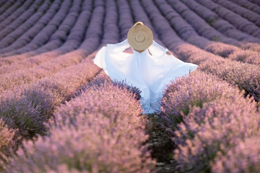 Happy woman in a white dress and straw hat strolling through a lavender field at sunrise, taking in the tranquil atmosphere