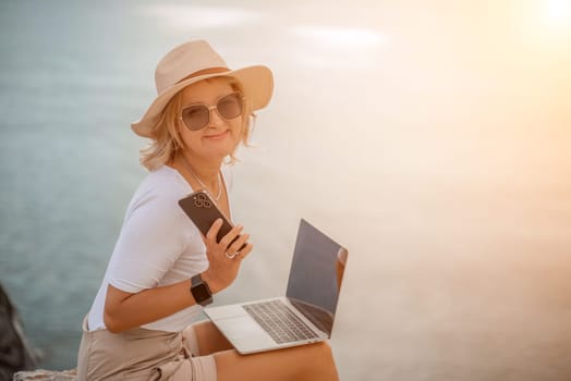 Freelance women sea. She is working on the computer, talking on the phone in the open air with a beautiful view of the sea. The concept of remote work