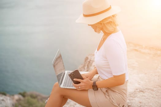 Freelance women sea working on the computer. Good looking middle aged woman typing on a laptop keyboard outdoors with a beautiful sea view. The concept of remote work