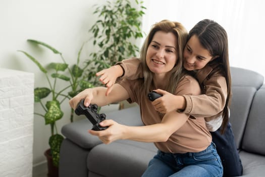 Happy family together. Mother and her child girl playing video games. People having fun at home.