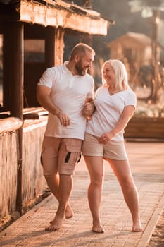A happy married couple in shorts and T-shirts walks down the street at sunset in summer.