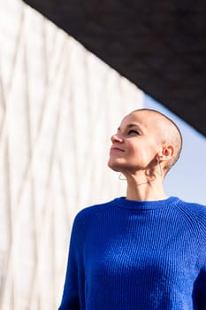 empowered woman with bald head smiling looking to the sky at city, concept of urban lifestyle and rebel style, copy space for text