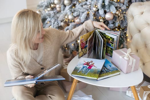 Beautiful young woman is looking her old photo album while spending Christmas alone at home.