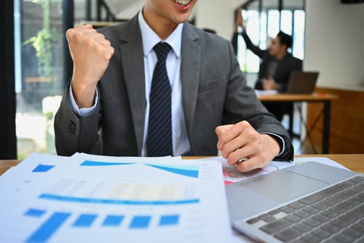 Cropped shot of male worker looking at laptop screen, making winner yes gesture, celebrating business success.