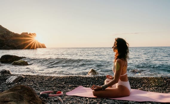 Young woman in swimsuit with long hair practicing stretching outdoors on yoga mat by the sea on a sunny day. Women's yoga fitness pilates routine. Healthy lifestyle, harmony and meditation concept.