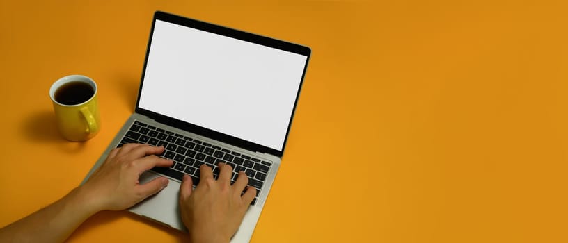 Shot from above view of unrecognizable hands typing on keyboard of laptop computer over yellow background.