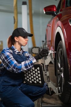 A female auto mechanic makes a camber. Woman working in a car service