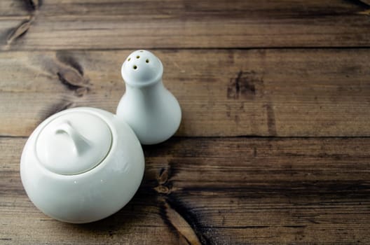 Sugar bowl and salt shaker on a wooden table. Ceramic sugar bowl and salt shaker on a dark wooden table close-up.