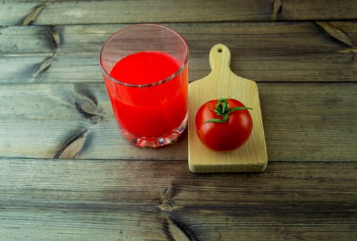 Tomato and tomato juice on a dark wooden table. Tomato and tomato juice in a glass on a dark wooden table close-up.