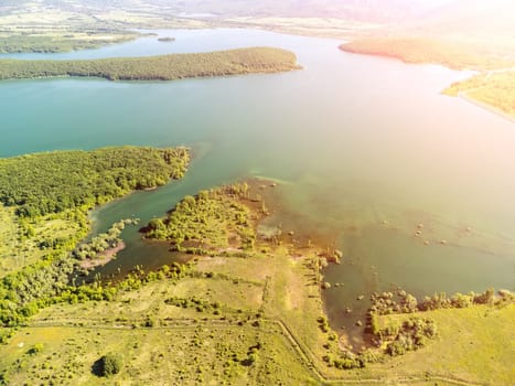 Aerial landscape from flying drone storage reservoir at mountain foot covered colorful spring forest. Beautiful view from above blue lake among highlands