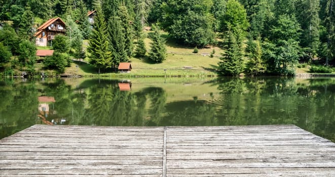 Wooden board, empty in front of blurred lake and house in forest. Perspective brown wood over blur in outdoor - can be used for display or montage your products.Mock up for display of product. download photo