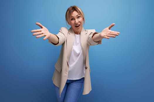 smiling blond young adult in jacket pulls hugging on studio background.