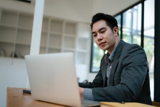 Portrait of an Asian male business owner standing with a computer showing happiness after a successful investment.